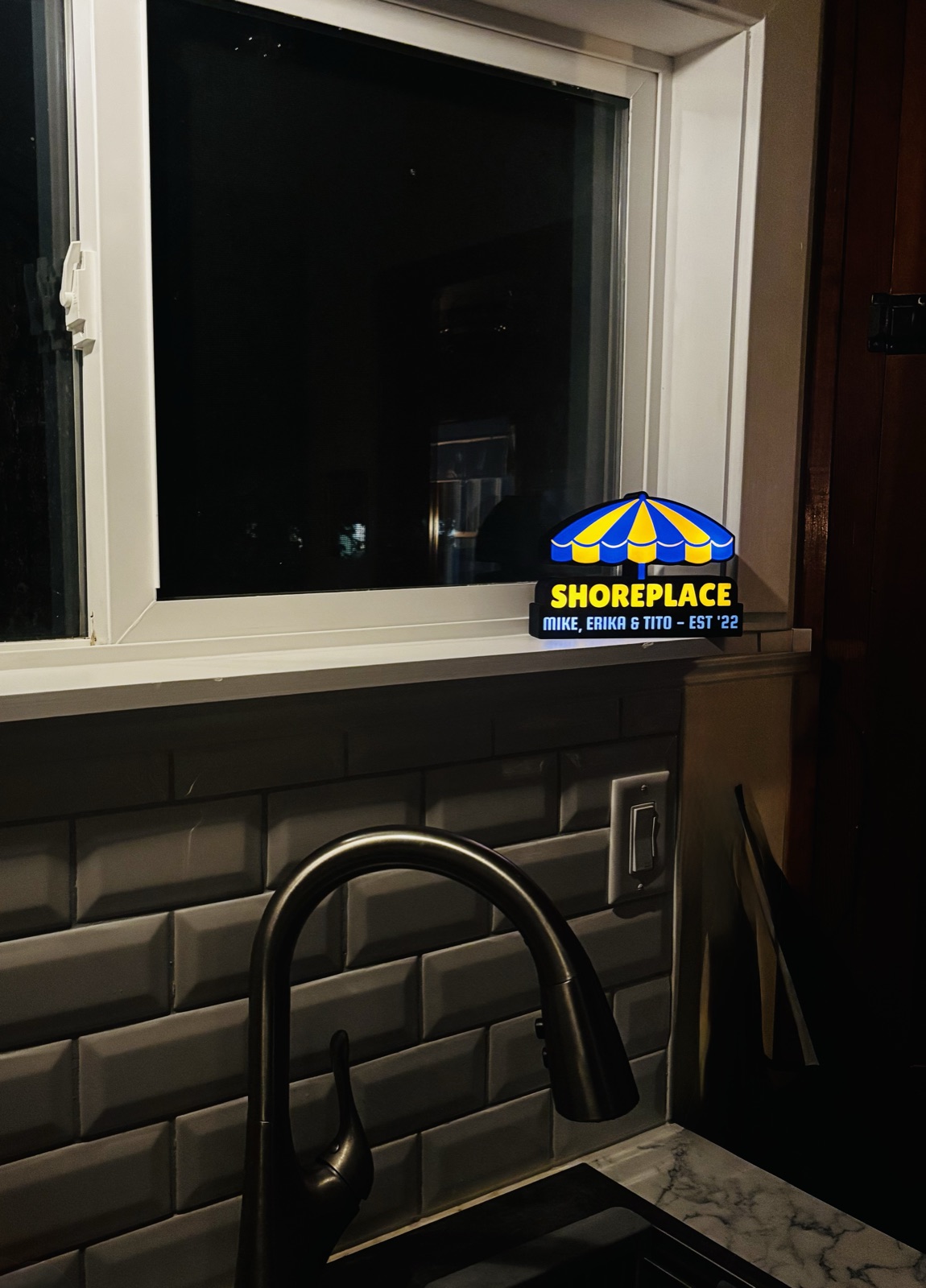 The Shoreplace lightbox glowing on a kitchen windowsill above the sink.
