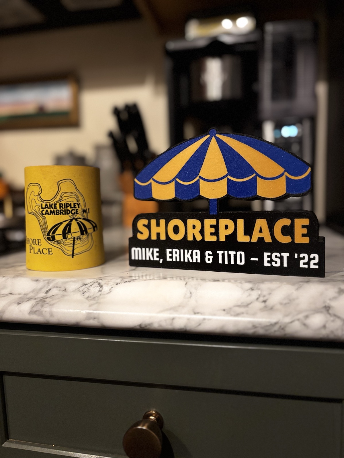 The Shoreplace lightbox unlit on a marble kitchen counter next to a vintage Shoreplace koozie.